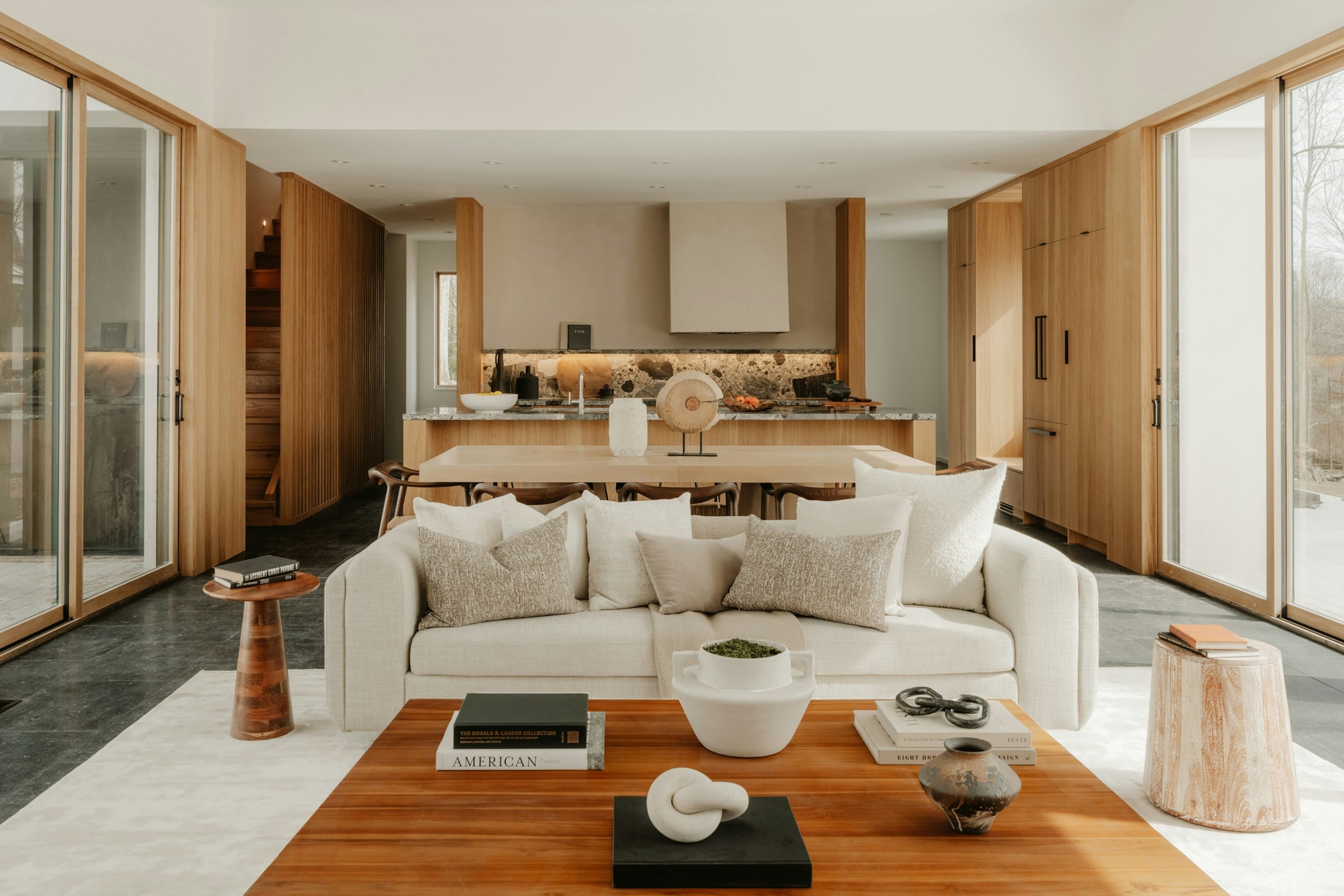 Sunlit living room with a cream sofa, a walnut coffee table and warm oak joinery opening onto the kitchen beyond