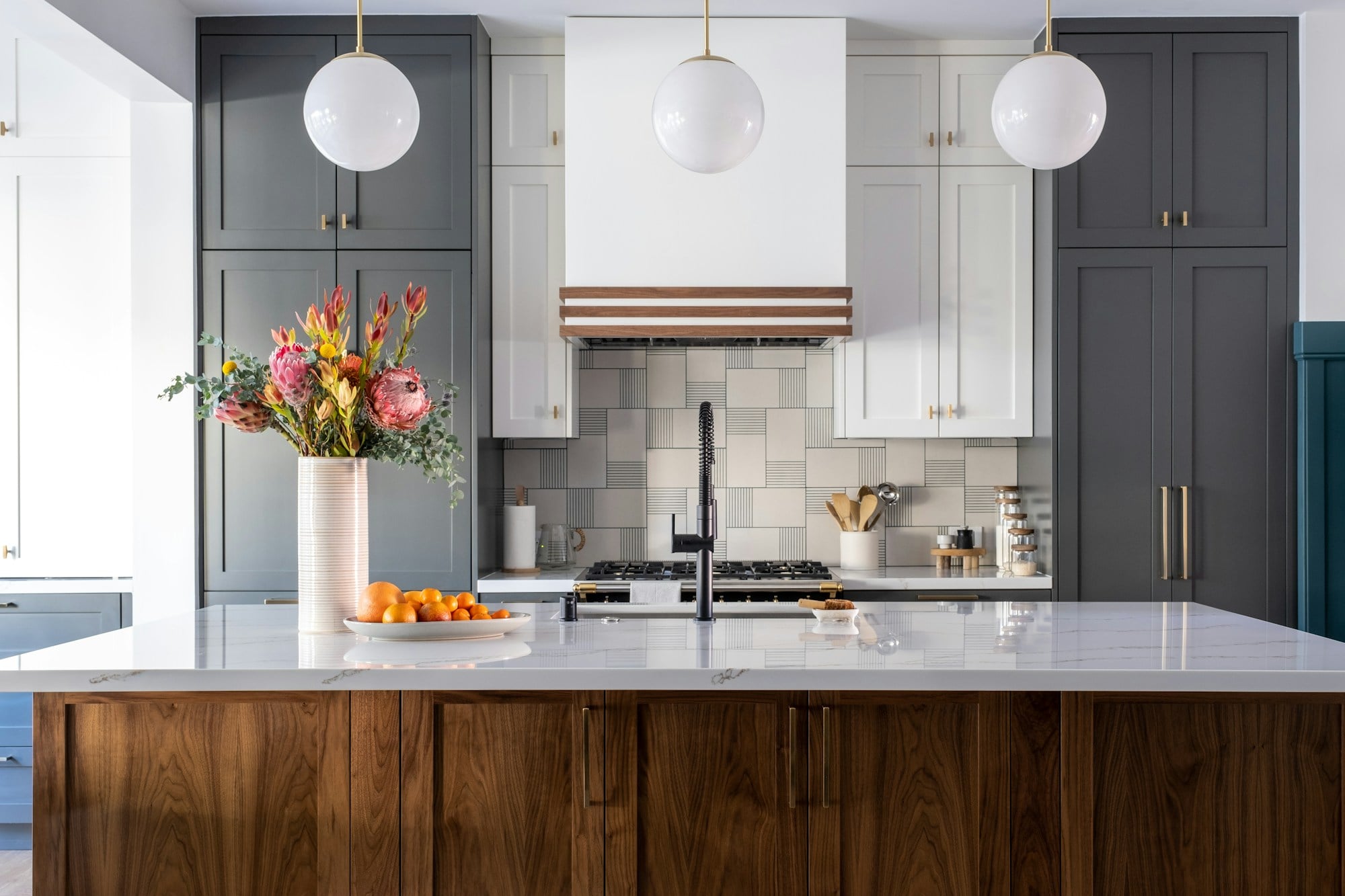 Fitted kitchen with a walnut island, a pale stone worktop, grey cabinetry and globe pendant lights